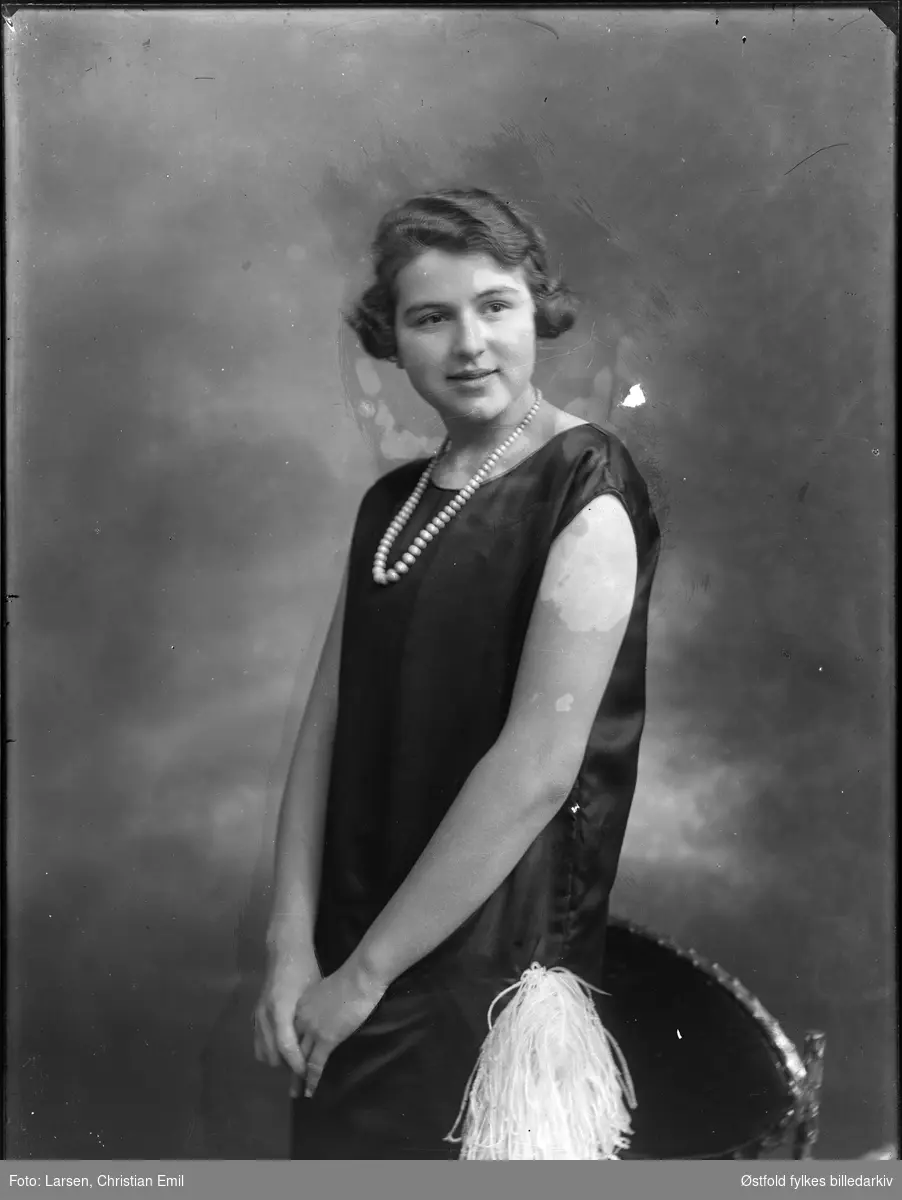 Portrett av ukjent ung kvinne med bobfrisyre, Charleston-kjole med fjærpynt og perlekjede, fotoatelier, 1926.