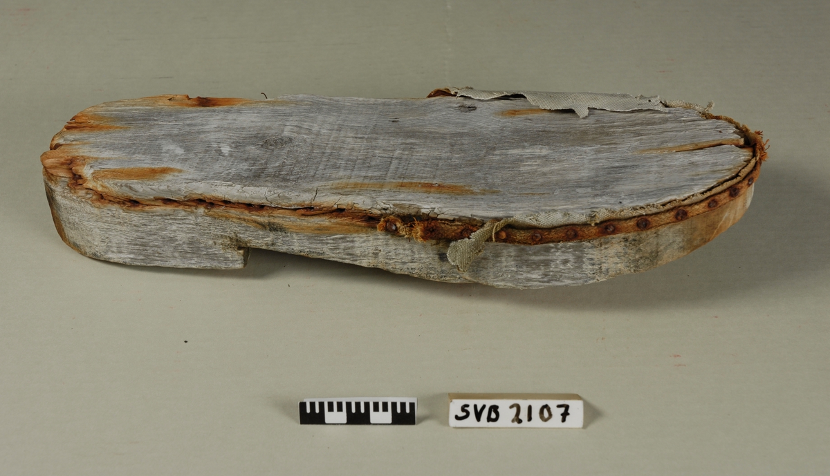 Såle av tre med rester av "overlær" i seilduk som har vært stiftet på med en rundvevd snor av tekstil