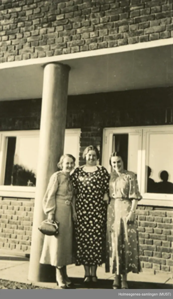 Tre unge kvinner foran en mursteinsbygning.