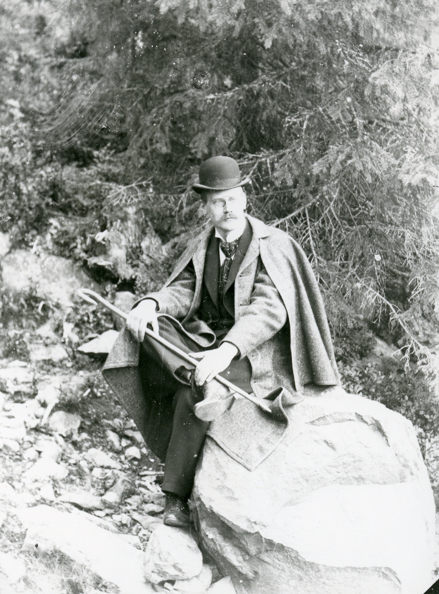 Mann med hatt, sittende på stein i skog