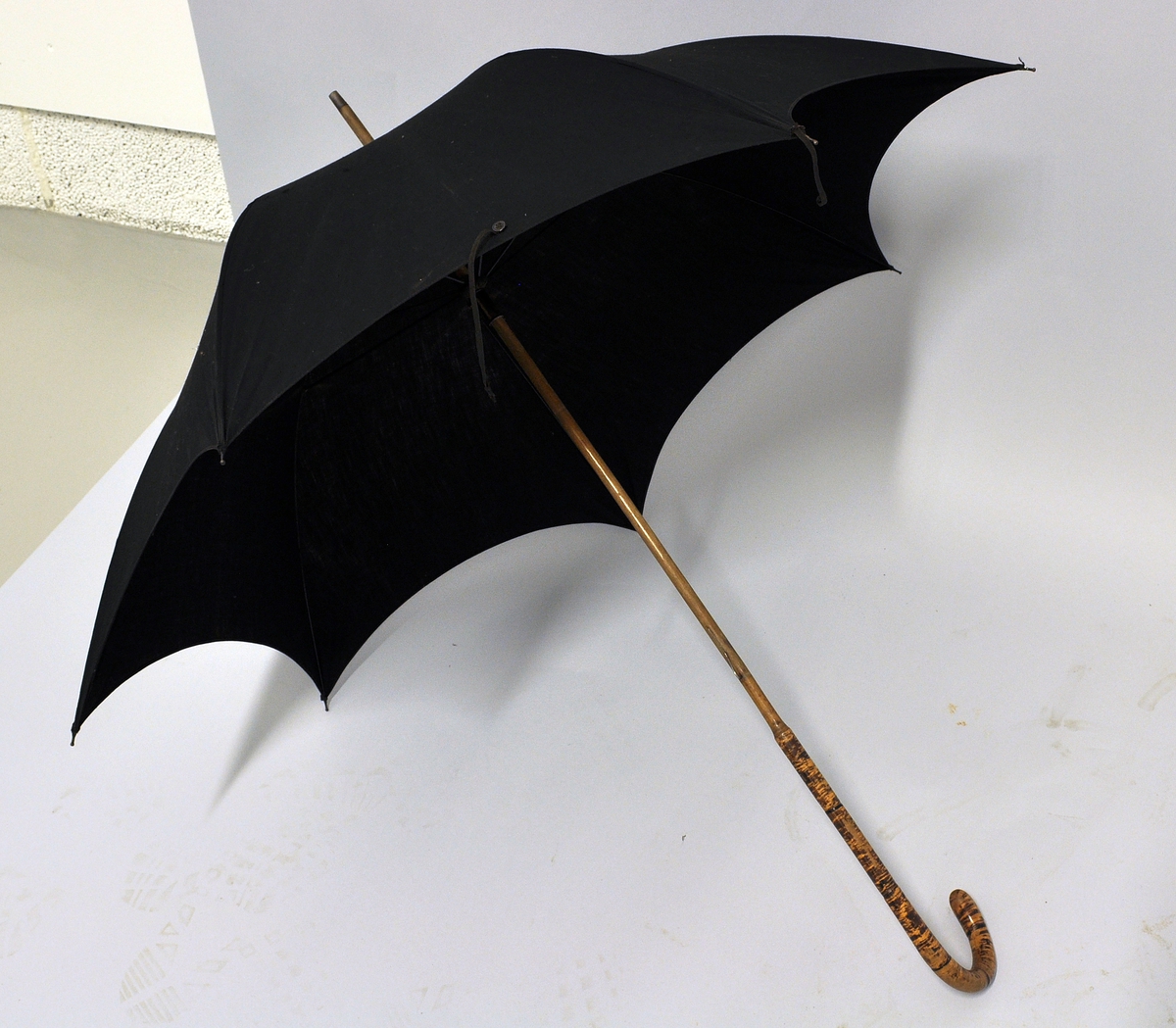 Sort stoffparaply med bøyd håndtak av tre.