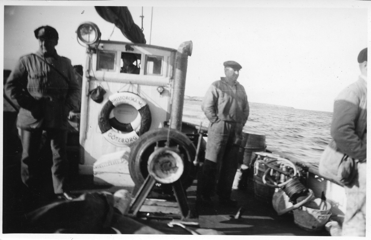 '3 män ombord på båtdäcket på ''Skandia'' i Sotenkanalen. Livboj med texten ''Naturhistoriska museet''. ::  :: Ingår i serie med fotonr. 3441-3452.'