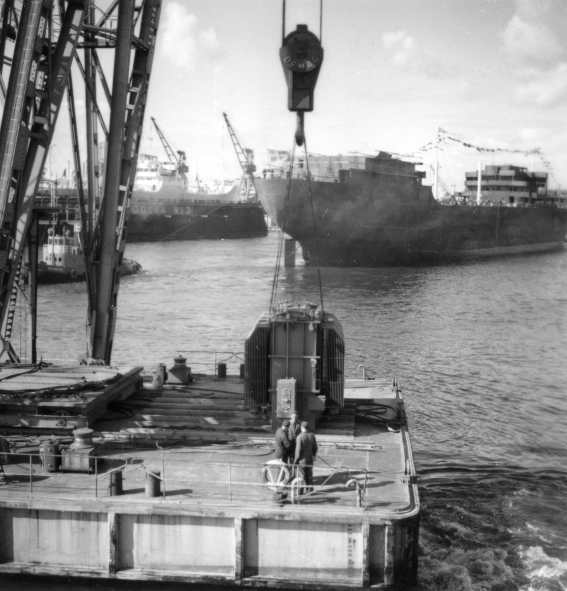 Transport av transformator 50 kW på Göteborgs hamn, 17/6-1955. Arbetspråmen är CHAPMAN som ägdes av Göteborgs hamn. Några män är med på bilden. Bogserbåten i bakgrunden är Röda Bolagets isbrytande bogser- och bärgnings(ång)båt HERBERT byggd på Eriksberg 1944.  Den sjösatta tankern är M/T FERNCOURT och sjösättningen skedde16/6 enligt upggifter från Eriksbergs varvs arkiv och det sjösatta skrovet är under bogsering till en av utrustnings/reparations pirerna som ägdes av Eriksbergsvarvet.  M/T Ferncourt var en 17 3/4 knops 9000 tonnare med en tonnagedödvikt (twd) på 24 400.
Beställare var Olsoredeiet Fearnley & Eger och levernasen skedde 7/9-1955. Den var den första av fyra fartyg som leverades i följd till samma rederi.  Bilden är tagen från Majnabbehamnen.