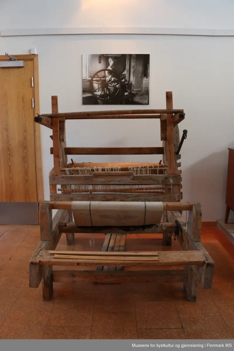 Vevstol fra før Andre Verdenskrig i umalt treverke, med deler av metall og bambuspinner. Tøystykke med hakekors medfølger, pga at disse har vært utstilt sammen.