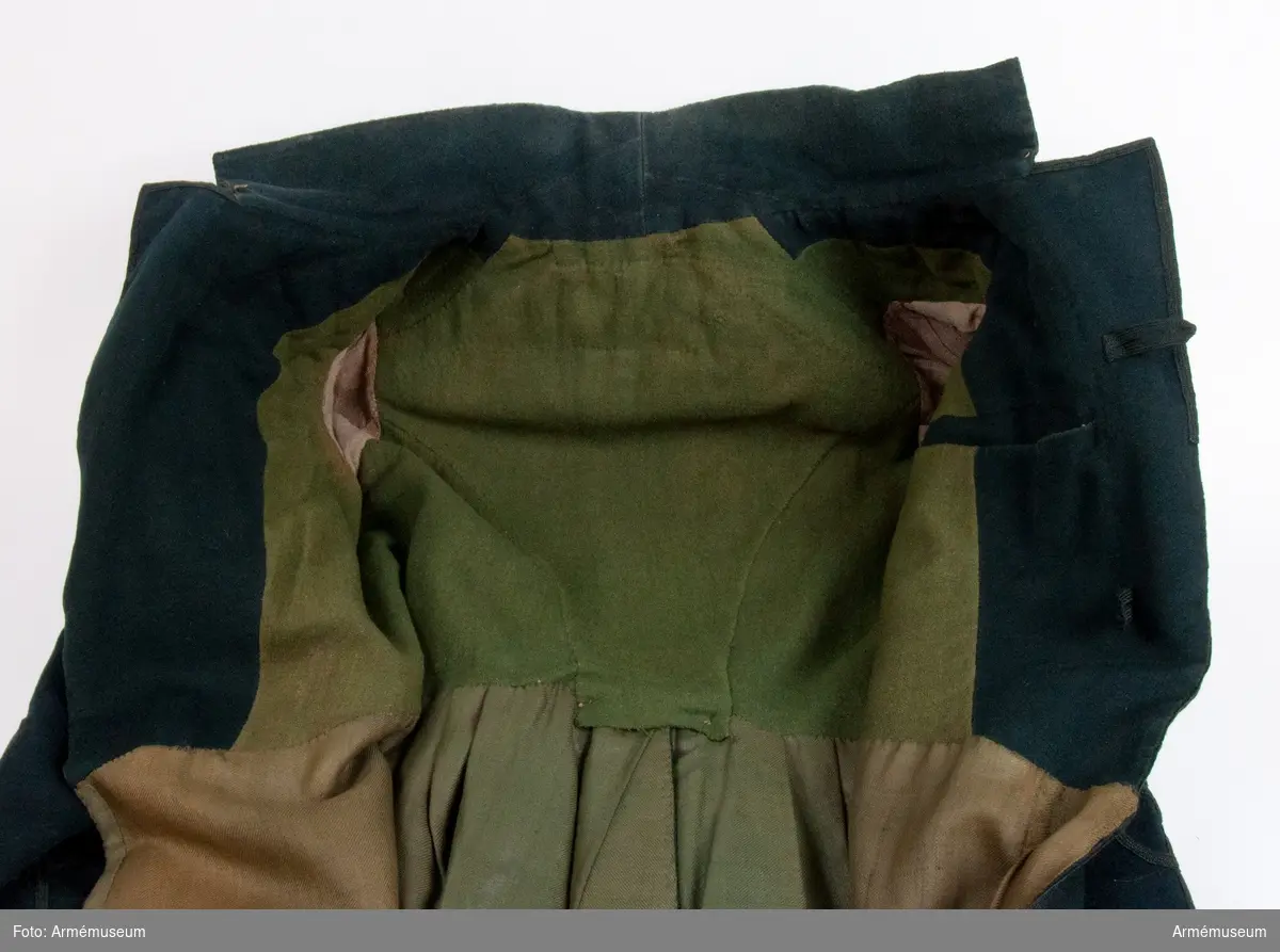 Grupp C I.
Bigeschen är tillverkad i mörkgrönt kläde och fodrad med grön boj i livet, linne i ärmarna.