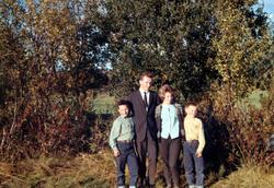Fire personer fotografert i terrenget med endel løvtrær bak 