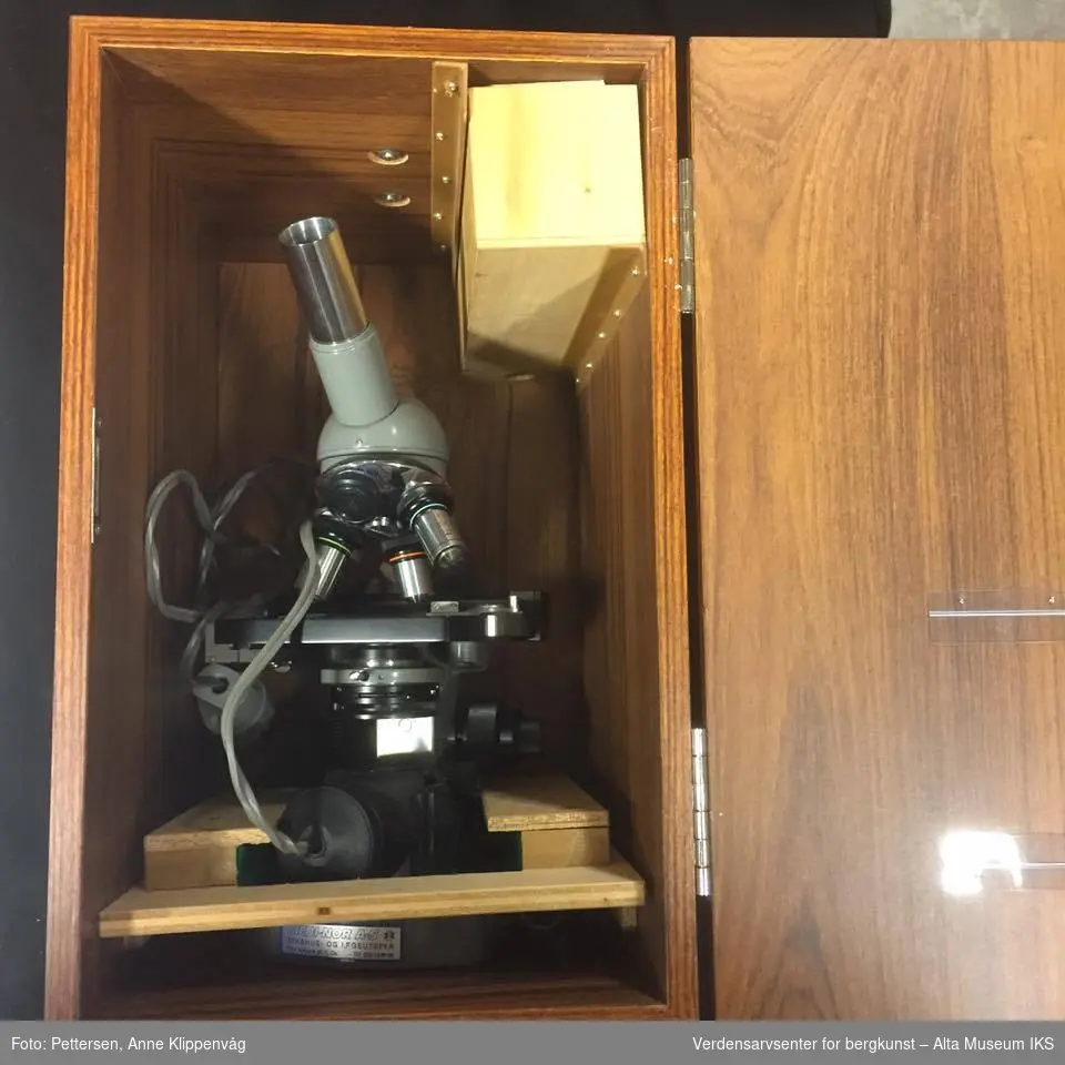 A: Trekasse, med bæreåndtak festet på oversiden. Inneholder et mikroskop, en ekstra trebunn som beskytter mikroskopet, og en liten trekasse med ekstradeler til mikroskopet. Kassen står på fire gummiknotter. 

B. Mikroskop. Et grålakkert mikroskop, av merket Olympus. Elektrisk, med innebygget lampe.