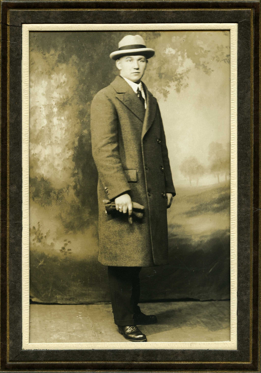 Portrett av stående herre i frakk og med hatt og hansker.