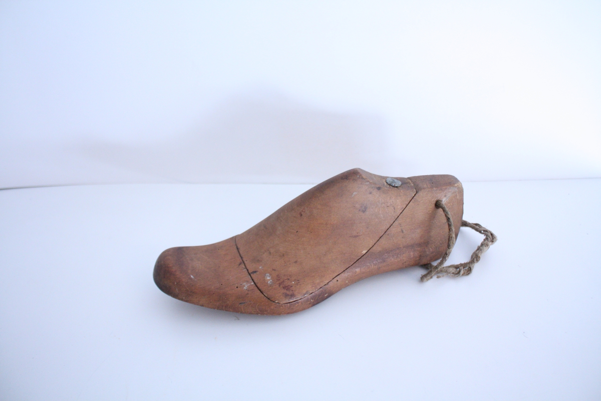 En venstre skoform. Skoformen er todel, der vristen er et løst stykke som holdes på plass med en spiker. Et tynt tau er festet gjennom et hull på hælen.