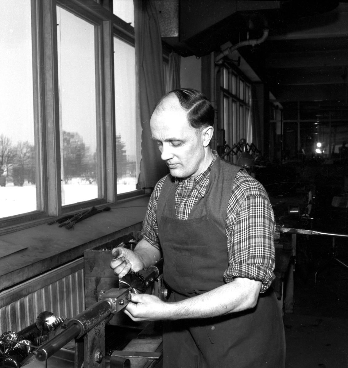 En man sitter vid en maskin och arbetar på Huskvarna Borstfabrik.