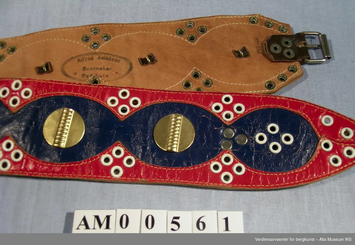 Belte sydd av rødt og blått skinn. Dekorert med 12 knapper av gullmetall og hvite maljer rundt.