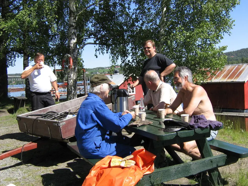 Foto av personer som sitter ved og rundt bord og har kaffepause.