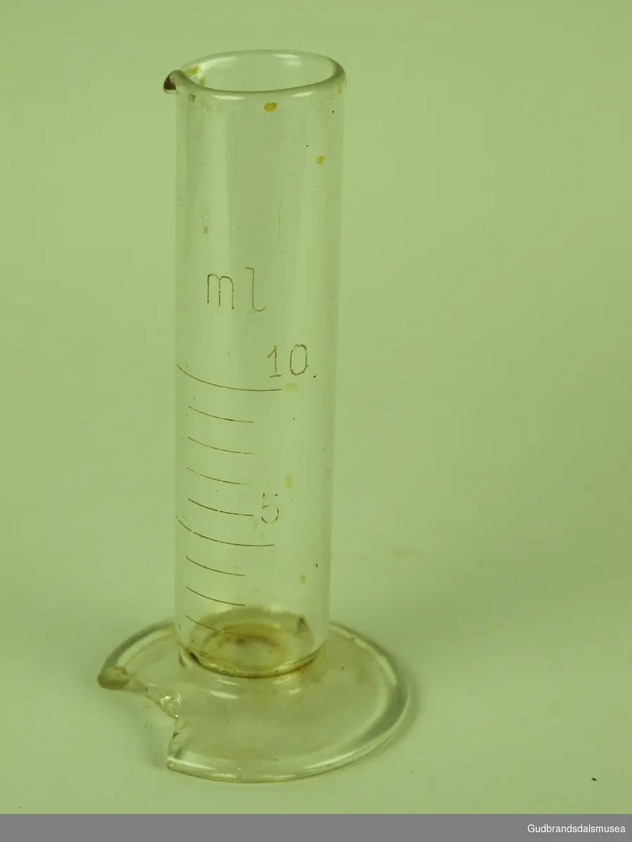 Laboratorieglass med tømmetut, samt måleskala på siden, glasset tar max 10 ml og har tall ved 5ml.