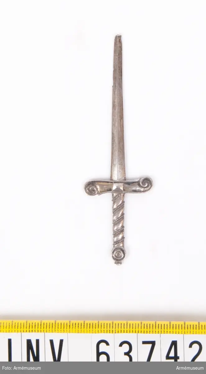 Grupp M II.
Ett svärd av silver med vridet ornetat fäste. I svärdets spets en liten ögla. Svärdet bars med fästet nedåt.