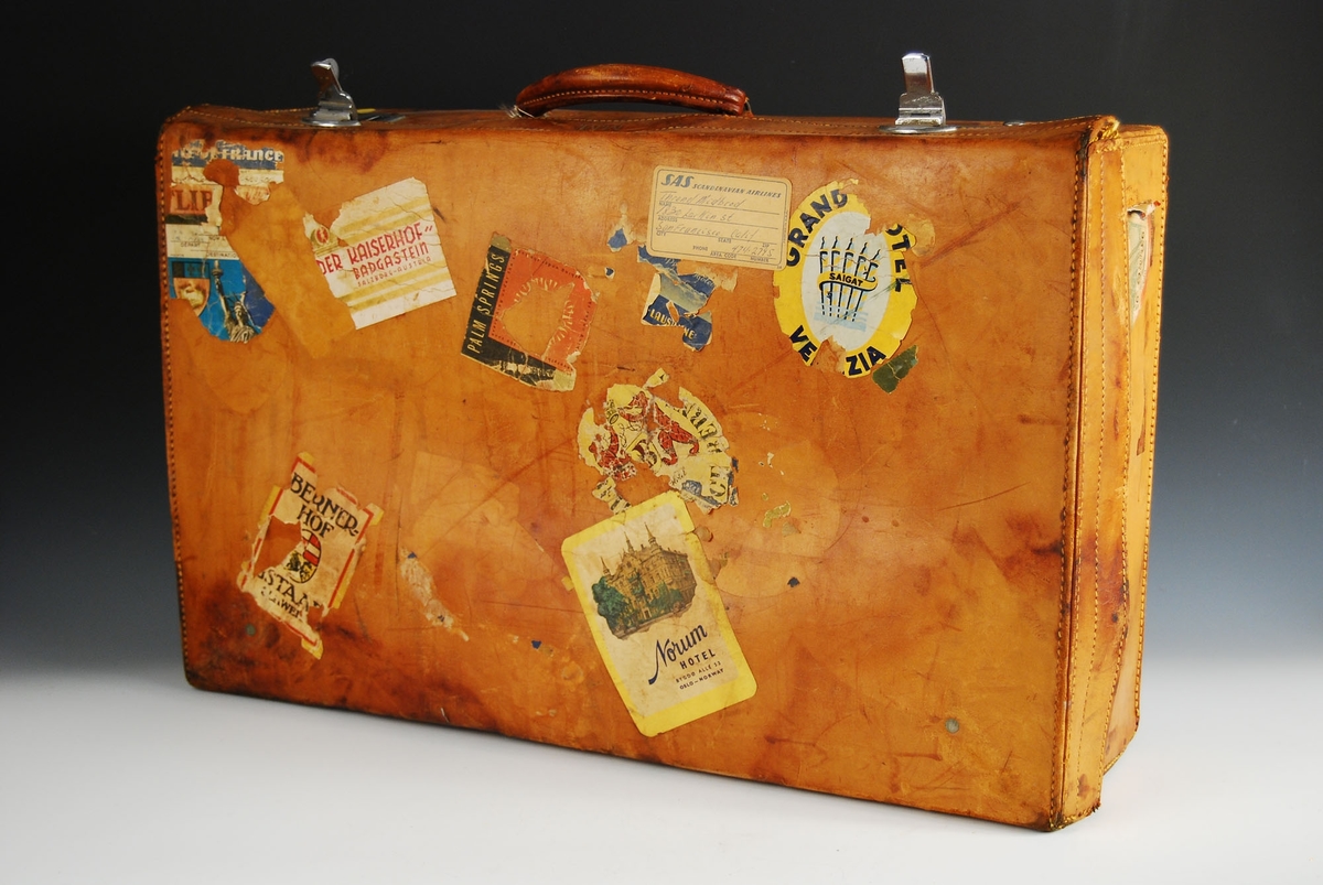 Koffert med to metallåser og håndtak av lær. Striefôr innvendig. 

Utvendig er det festet ulike klistermerker fra flere steder i verden.