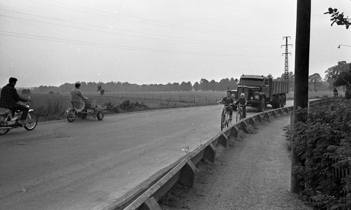 Popgala i Kumla, Farlig skolväg 24 augusti 1965

Två skolbarn på väg till skolan cyklar på en farlig väg trafikerad av en lastbil, en moped samt en flakmoped bl.a.