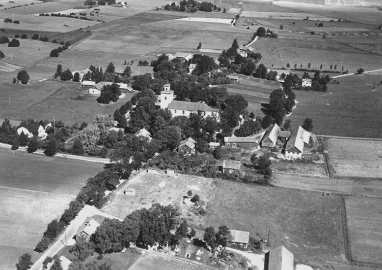 Flygfoto över Tysslinge kyrka, bostadshus och ekonomibyggnader.
Bilden tagen för vykort.
