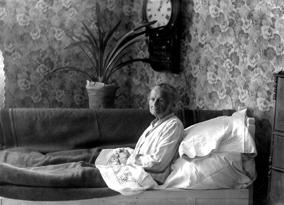 Rumsinteriör, en äldre kvinna i sängen.
Clara Gustava Gustafsdotter (född 1833-08-24) vid Kratorpsviken i Svennevad på 100-årsdagen.
(Sigrid Hallbergs farmor).