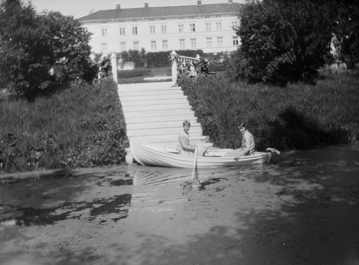 To kvinner i en robåt på dammen i hageanlegget på Linderud Gård. I bakgrunnen sees hovedbygningen.
