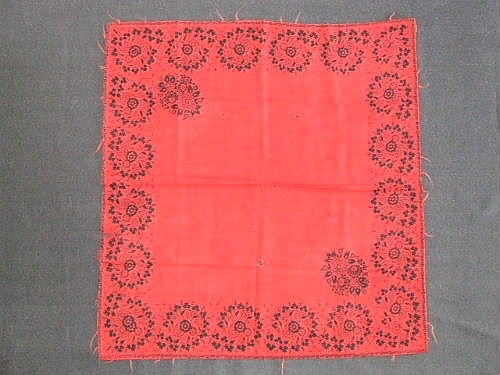 Schal av rött ylletyg med tryckt mönster i  form av svart blomsterbård runt om. Fragment av frans i rött ullgarn på sidorna. Handfållad.

Sökord: ull.