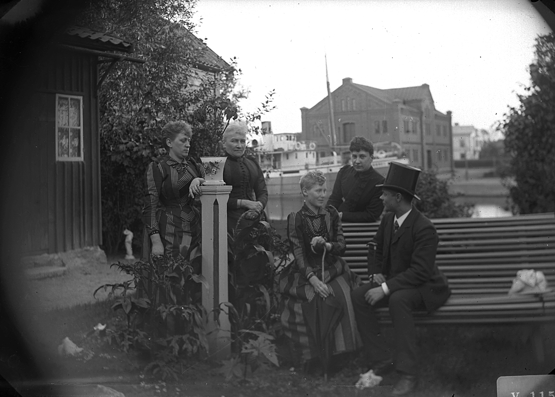 Grupp fem personer.
Bostadshus till höger på bilden. Hamnmagasinet i bakgrunden.
Bilden är tagen ca 1890 (hamnmagasinet byggdes i slutet av 1880-talet).