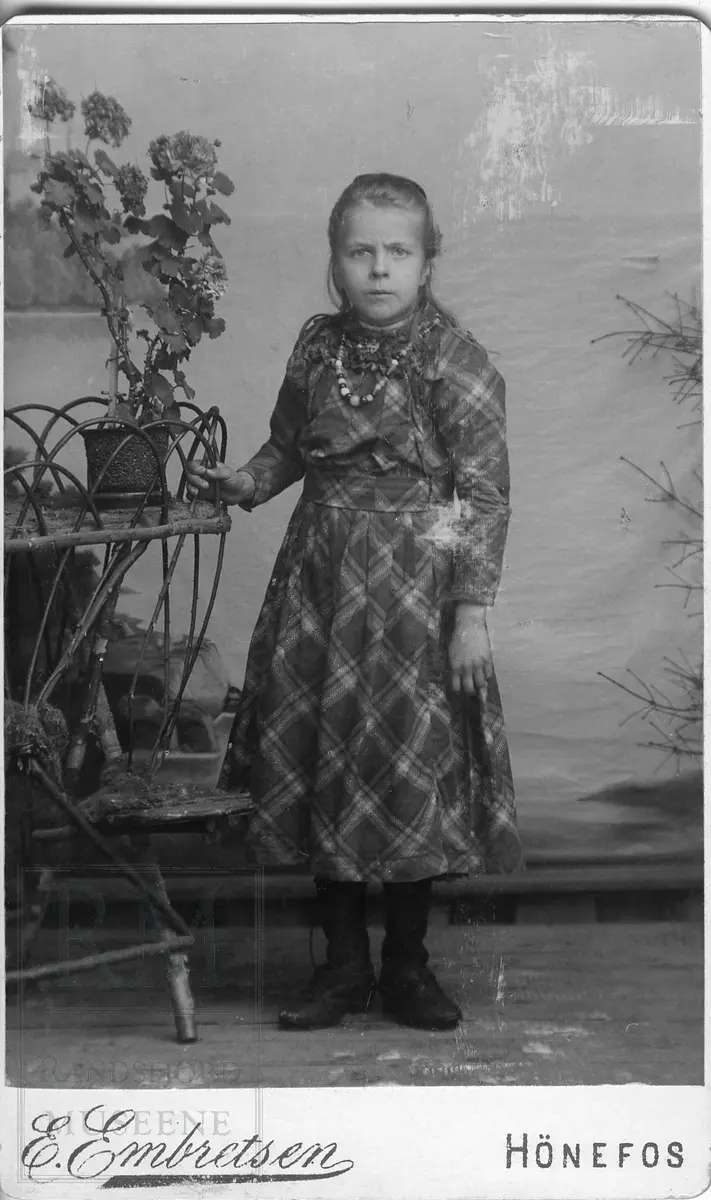 Ei jente stående ved et blomsterbord. Jenta er Gunda Kristiansdatter Bølhaugen, f. 18.4.1889