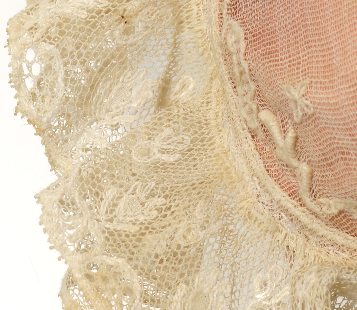 Dåpslue, kysefasong som kvinnekyser fra 1830 årene:  Tyll med små firbladblomster og grenbord langs kanten, rynket til sirkulært felt på issen. under tyllen rosa  silke. Langs kanten to tyllblondekapper over hverandre, over tinningene to sløyfer av lilla silkebånd knyttebånd av samme. Sløyfene har små tøyblomster.