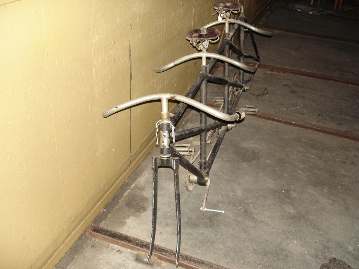 Tresitsig cykel. Lösa delar: tre styren, tre sadlar och tre par pedaler. Flera delar fattas. Axelavstånd: 2280 mm. Ramens höjd: 770 mm.