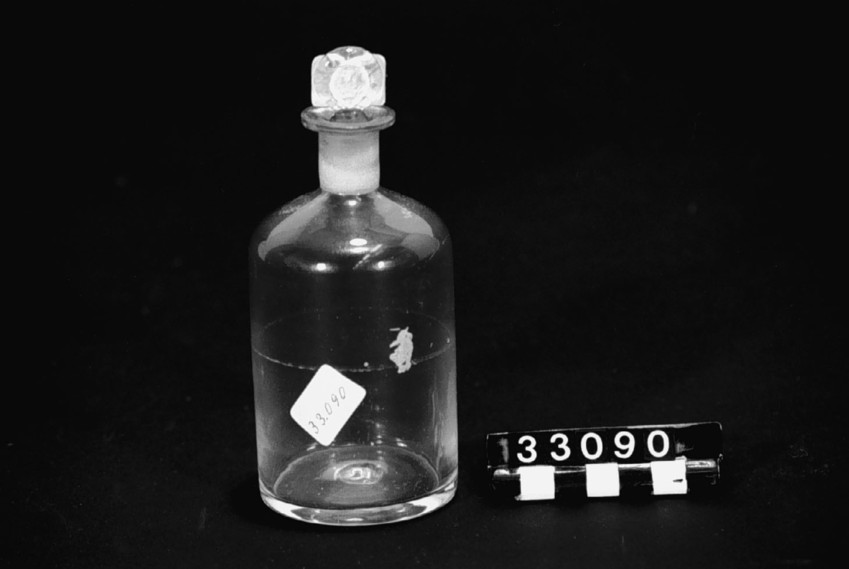 Apoteksflaska med inslipad propp, av ofärgat glas, handblåst, med tillplattad propp, rund snodd i formen.