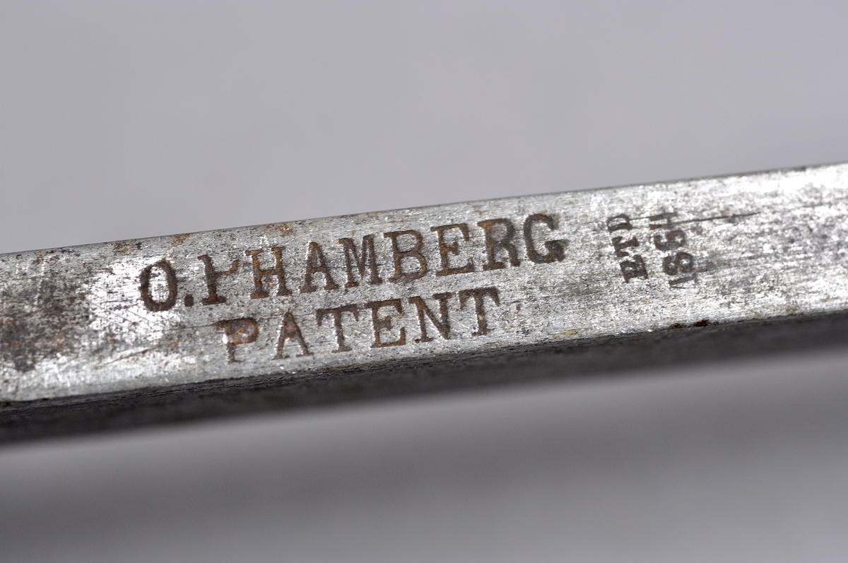 Besman av järn komplett med krok, järnklumpen är rund. Märkt/justerad: AFH 1863. O Hambergs patent, med trähandtag. Tillverkad av RTD 1864.