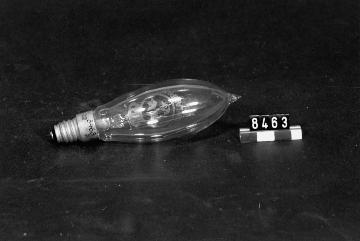 Elektrisk glödlampa med metalltråd, "Kronlampan", mignonfattning. Märkt: "22 K 12 x 78 16" samt lilla riksvapnet och därunder "kronlampan".
