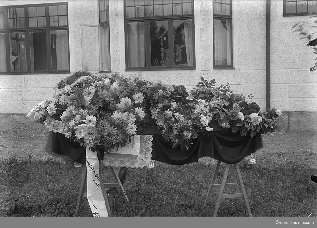 Begravning, likkista och blommor. Bostadshus.
Bilden är tagen utanför fastigheten Elinsberg, Ullersäter. Där bodde Nanny och Karl Jansson. Nanny Jansson avled i slutet av 1930-talet.
Se även bild 2008:35:21.