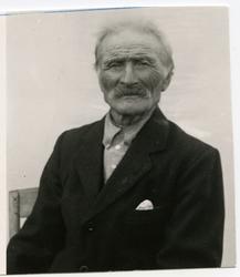 Portrett av en eldre mann som sitter på en stol. Mannen er i