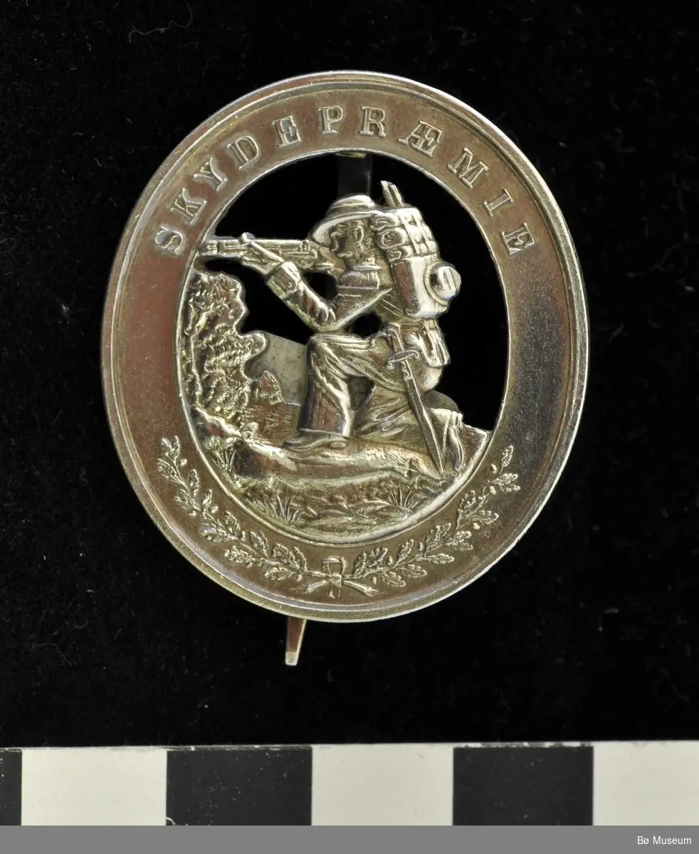 Oval medaljenål med motiv av en knestående skytter