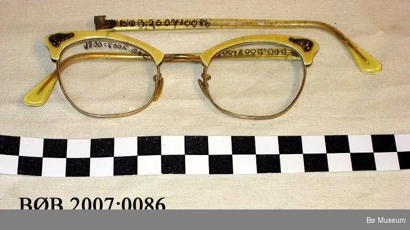 Damebriller i metall og plast med ein liten krusedull på kvar side til pynt.