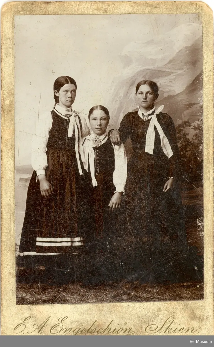 Tre yngre kvinner i vesttelemark-drakt i fotoatelier.
Kvinna t.h. er Liv O. Nørsthaug, gift Tjønntveit i Øvre Bø.
Dei andre er to venninner.