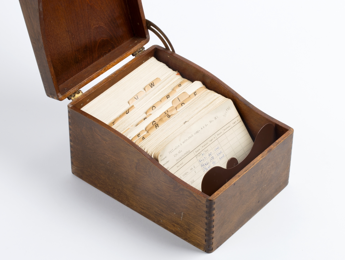 Laboratoriejournal i kasett. Kasett i løvtre, brunbeiset og polert, rektangulært eskeformat. Lokk hengslet i bakre kortside, forskyvbar støtte for kartotetkort.
Innhold: Kartotekkort med oppskrift for tilvirkning av ulike legemidler.