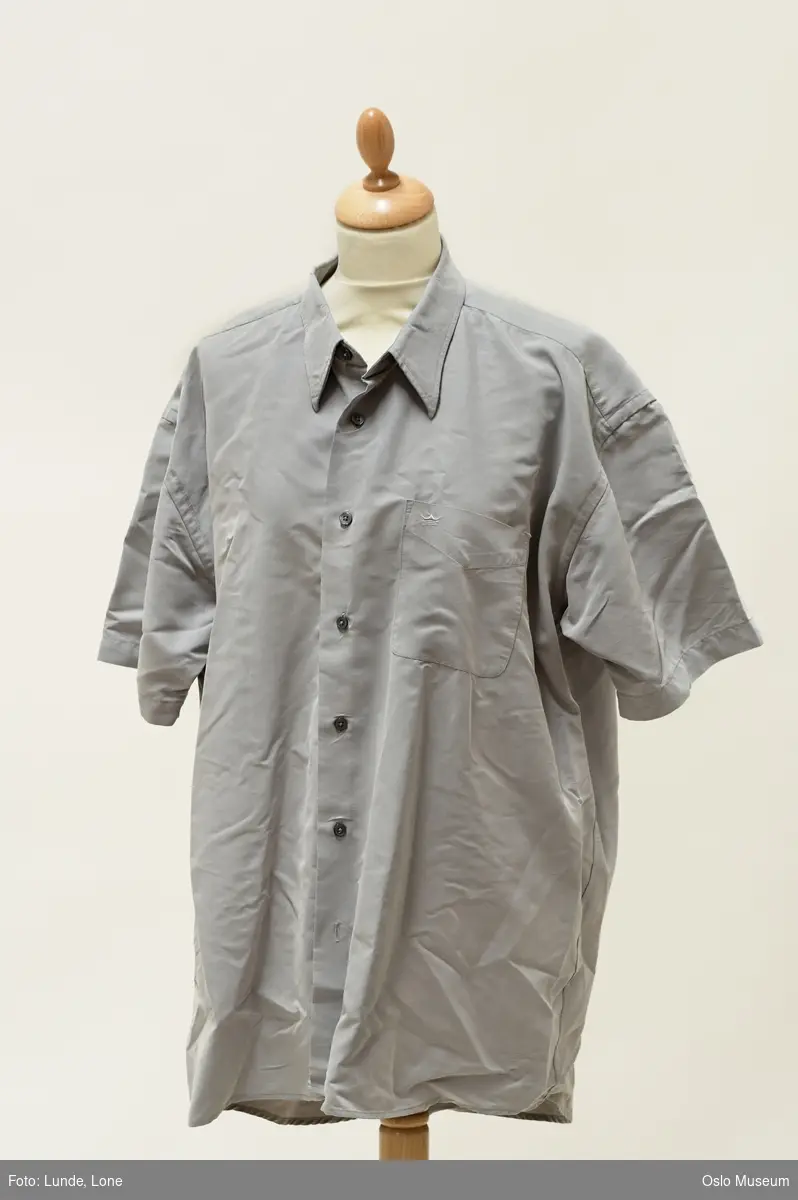 Kortermet herreskjorte i lysgrått kunstfiberstoff, brystlomme.