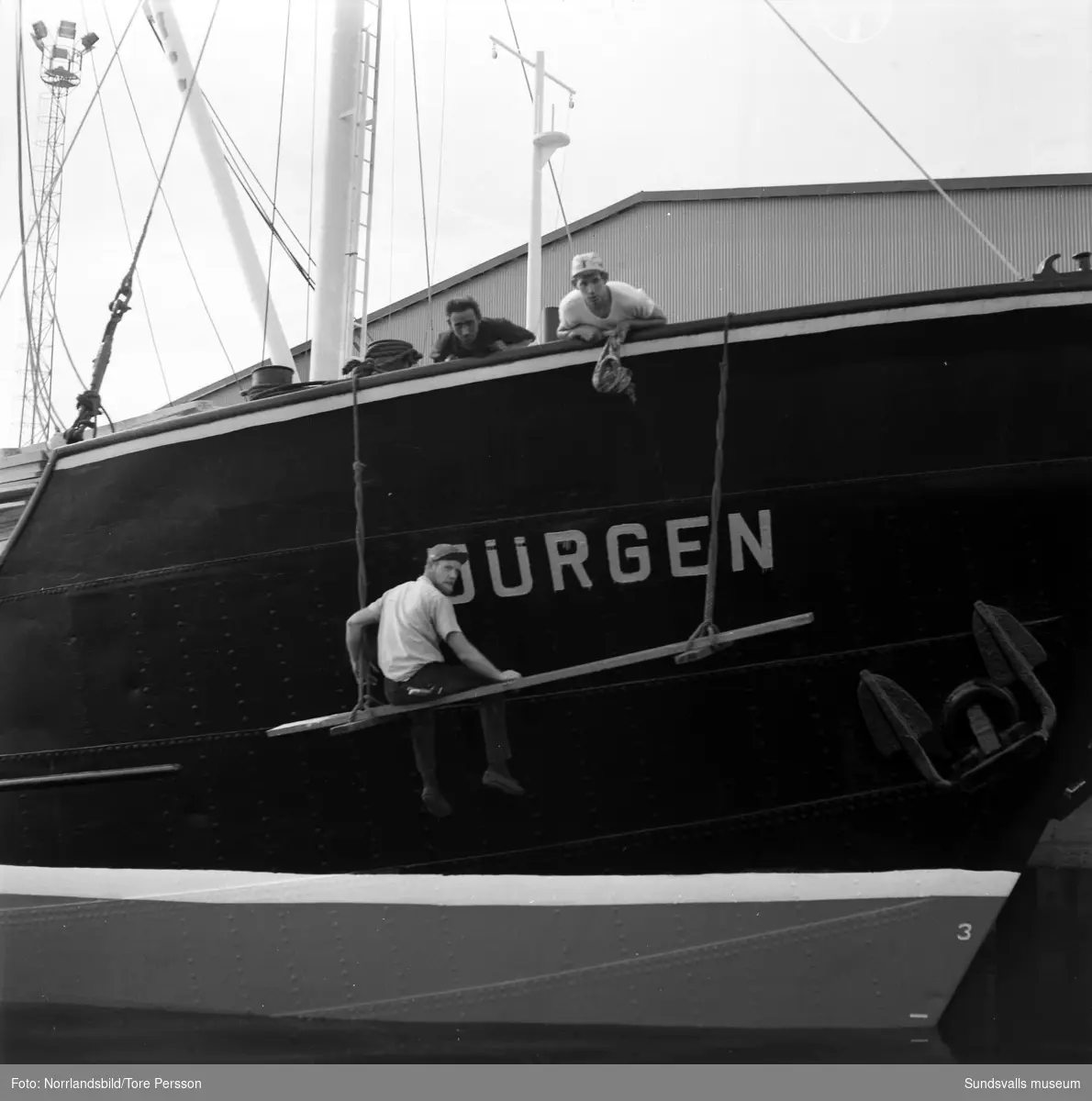 Tunadals sågverk fotograferad från sjösidan. Vid kajen lastas båten Jürgen med sågade trävaror.