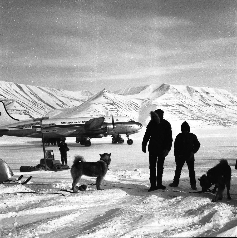 Lufthavn/Flyplass. Adventdalen/Svalbard. Et fly, LN-SUP, Douglas C-54B, Skymaster fra Braathens SAFE, har landet. To personer og to hunder betrakter flyet.