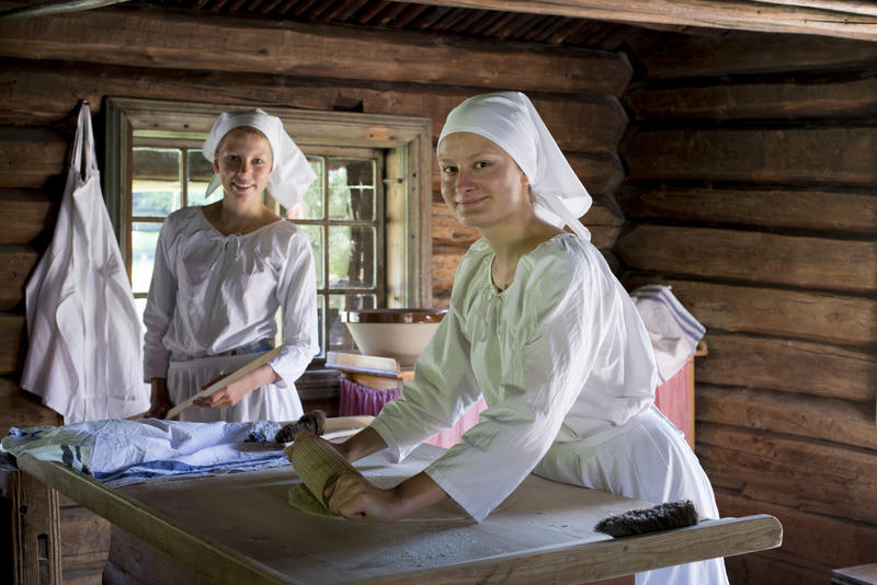 To kvinner baker lefser i eldhus