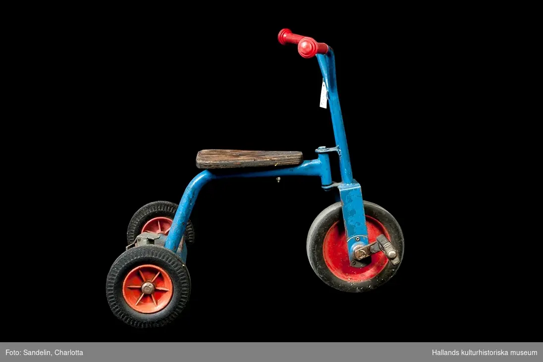 Röd och blå trehjuling med plasthandtag och träsits.