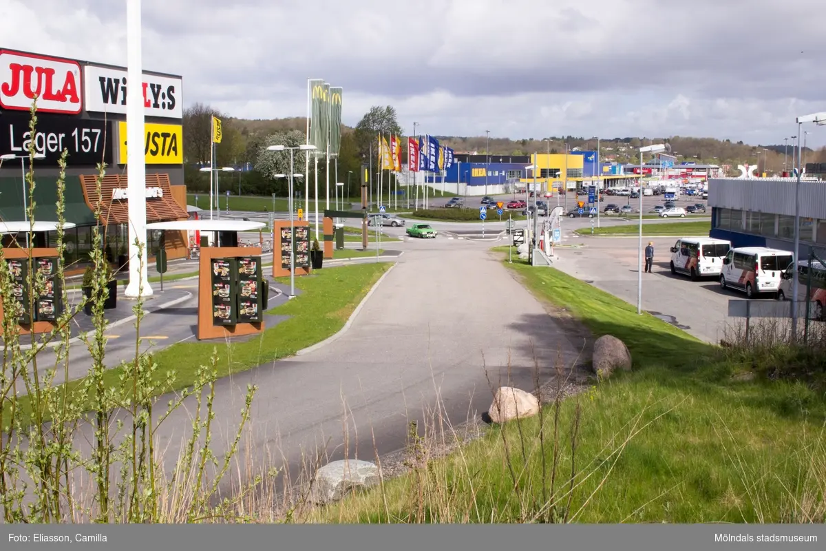 Vy från Ekenleden 1-3 i nordlig riktning mot IKEA. Till vänster ligger Ekens affärscentrum med bl.a McDonald's, som när den byggdes var Sveriges mest moderna och dygnetruntöppna restaurang. På höger sida ligger bensinstationen OKQ8 med tvätt, servicebutik och verkstad.
