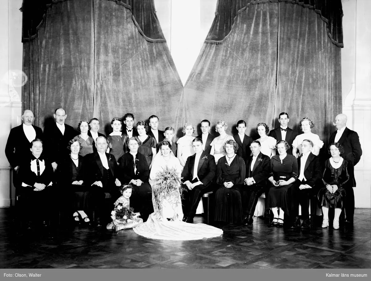 En gruppbild i bröllopsammanhang med ett brudpar i mitten. Enligt Walter Olsons journal är bilden beställd av ingenjör M Minqur ifrån Orrevägen 6 i Oskarshamn.