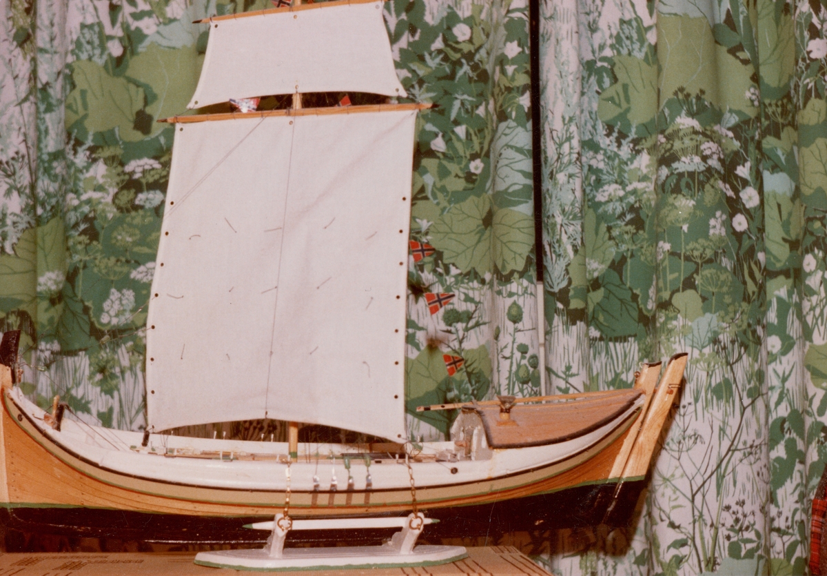 Modell av nordlandsbåt, fotografert med 70-tallsgardiner i bakgrunnen.