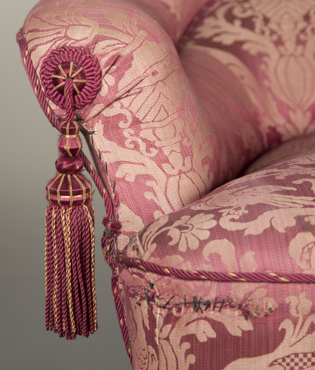Det symmetriske og gjentakende motivet på stoffet til sofaen er preget av bladverk, blomster, fugler og urner.