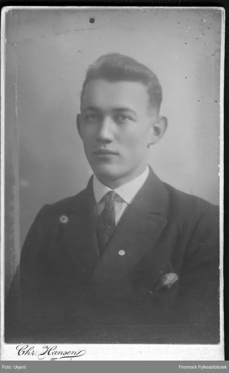 Portrett av en ung man antagelig fra Langfjordhamn i Loppa kommune. Han er kledd i dress: jakke, skjorte og slips. Han har trolig et tørkle i lommen. Bildet trolig tatt rundt 1900-1920.