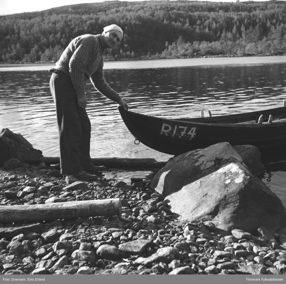 Søren Gabrielsen står foran baugen på en elvebåt ved bredden av en innsjø.