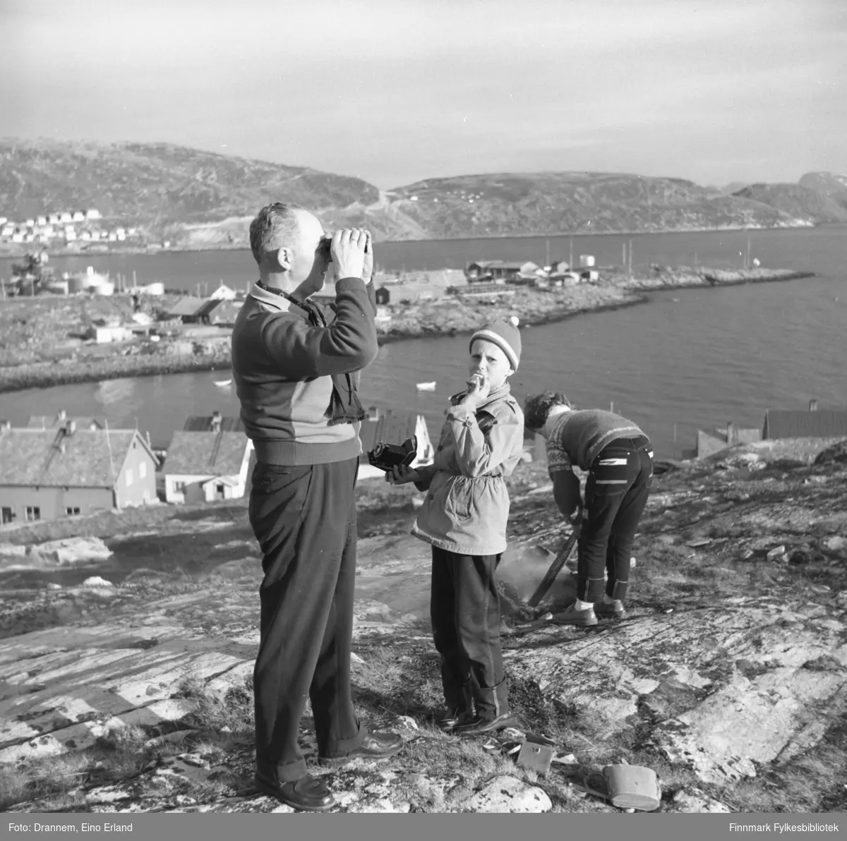 Tre personer i terrenget ovenfor Fuglenes. De er fra venstre: Olav Sørensen, Gunnar Sørensen og Turid Karikoski. Fuglenesodden stikker ut i sjøen midt på bildet.  Fotografiet kan være tatt på St Hansaften.