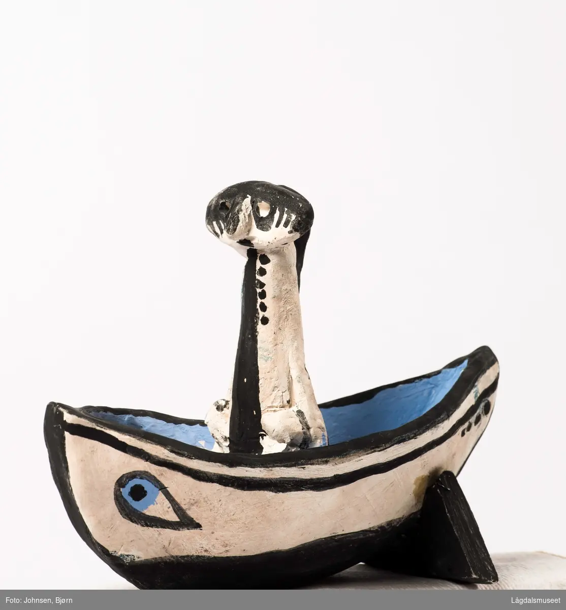Skulturen viser en mann i båt. Båten er dekorert med blå øyne.